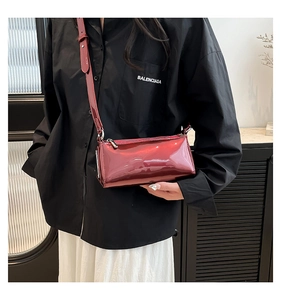 Detail of dark red patent leather cylindrical crossbody bag with shiny reflective finish