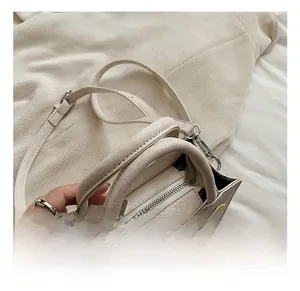 Détail du mini sac crème avec fermeture éclair argentée et doubles poignées cylindriques