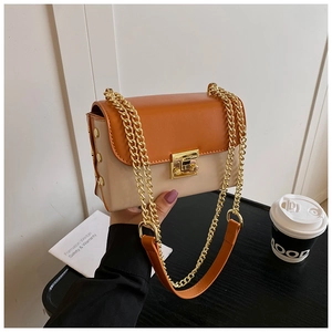 Detail of stylish beige and orange patchwork shoulder bag with golden chain and metal buckle