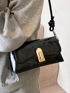 Chic black patent leather crossbody bag with golden metal twist lock shown on model