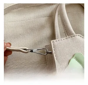 Détail du fermoir mousqueton en métal argenté et motif cœur vert sur sac beige texturé