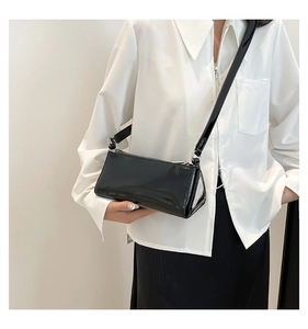 Close-up of black glossy patent leather baguette bag with silver metal hardware detail