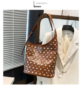 Détail du sac seau en cuir marron avec clous métalliques argentés et bandoulière réglable