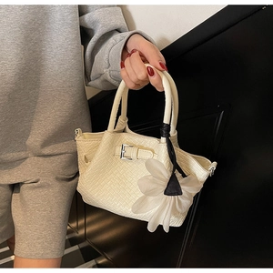 Détail du sac à main blanc cassé avec texture crocodile, boucle et breloque fleurie
