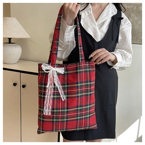 Detail of red and green plaid tote bag featuring delicate lace bow and pearl tassel accents
