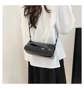 Detail of high-shine black patent leather baguette bag on model with white shirt