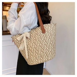 Detail view of woven straw tote bag with delicate white lace bow and brown leather strap