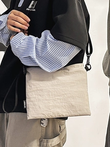 Sac bandoulière beige minimaliste à texture froissée et sangle noire porté par un mannequin