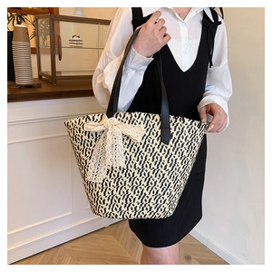 Close-up of woven straw tote bag featuring a large cream lace bow and black leather straps