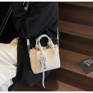 Detail of lychee pattern leather bucket bag in cream white with knot handle and charm