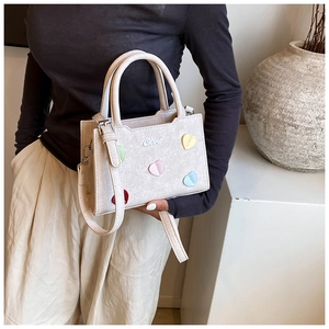 Détail d'un sac bandoulière crème chic avec patchs cœur colorés et finitions argentées