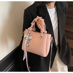 Side detail of pink lychee leather bucket bag with metal bow pendant and MaishaKele logo