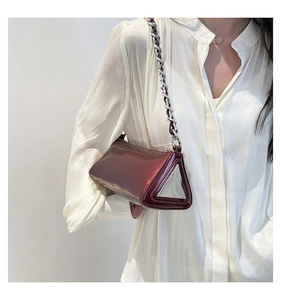 Detail view of burgundy triangle baguette bag with chain strap on a white silk blouse
