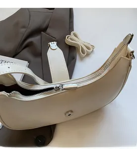 Detail view of cream crescent bag with silver zipper, magnetic closure and dual straps