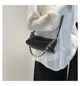 Glossy black baguette bag with silver chain detail shown on shoulder for daily styling