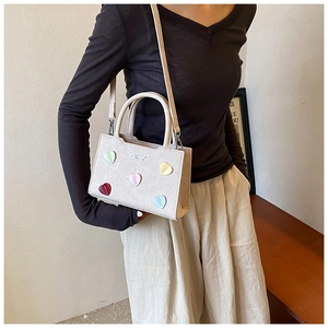 Détail des patchs en cœur colorés et logo sur le petit sac à main blanc