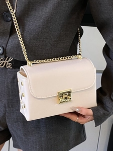 Elegant beige crossbody bag with gold chain strap and studs, styled on a grey blazer