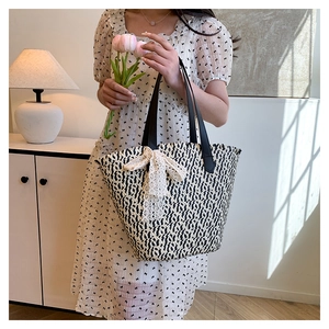 Detailed close-up of large woven straw tote with lace bow and black leather handles