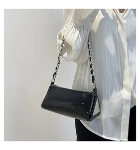 Detail view of black patent leather baguette bag with silver chain strap and triangular side