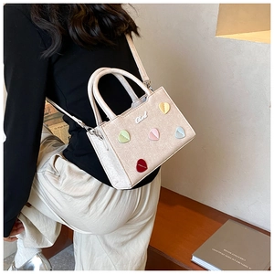 Détail du sac beige texturé avec écussons cœurs colorés et bandoulière amovible