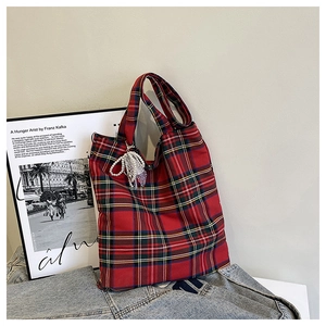 Detail of red plaid tote bag with pearl bow tassel charm on dark denim fabric