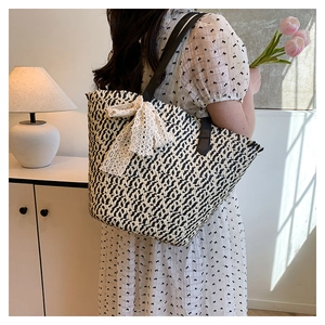 Detail of woven straw tote bag featuring a white lace bow and black shoulder strap