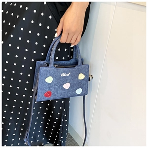 Détail d'un mini sac en jean bleu avec cœurs brodés colorés et logo argenté
