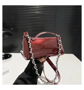 Macro view of burgundy patent leather baguette bag with silver chain and metal triangle