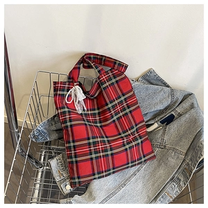 Detail of red plaid tote bag with pearl lace bow charm in a casual shopping cart setting
