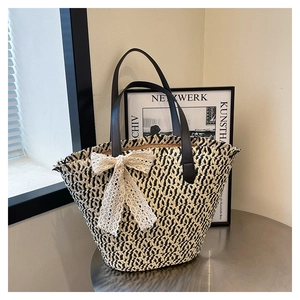 Detail of woven straw tote bag featuring a cream lace bow and black leather handles
