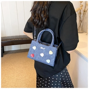 Détail du sac à main en denim avec écussons cœur colorés et finitions métalliques argent
