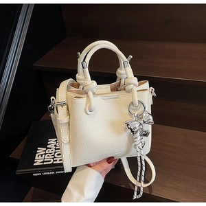 Detail of lychee textured leather bucket bag with silver butterfly charm on dark wood