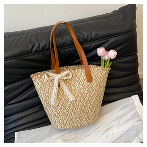 Close-up of woven straw tote bag featuring a white lace bow and brown leather handles