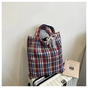 Detail of checkered tote bag with pearl lace bow charm on suitcase background