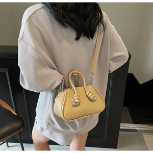 Dettaglio della borsa beige a grana litchi con nodo decorativo e finiture metalliche