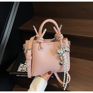Detail of pink lychee leather handbag featuring knot handle and silver heart charm