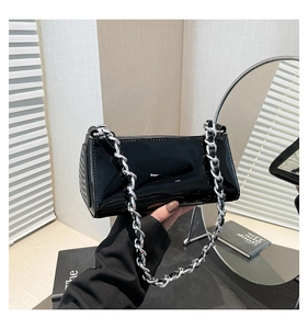 Close-up of black patent leather baguette bag featuring a thick silver chain strap