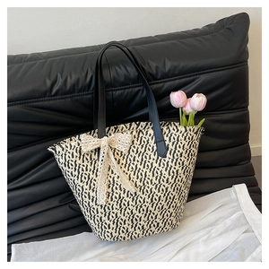 Detail of woven straw tote bag with black and white texture and beige lace bow