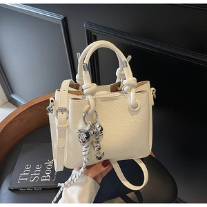 Detail of lychee textured leather bucket bag with silver cat charm and knot handles