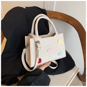 Détail du sac bandoulière crème avec patchs cœurs colorés 3D et logo métallique brillant