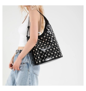 Détail d'un sac cabas noir avec clous argentés et cuir brillant porté par un modèle