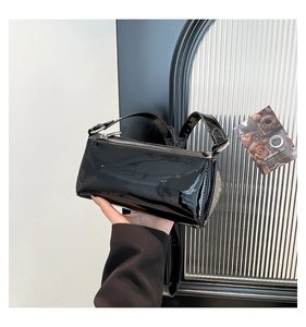 Detail of minimalist black patent leather baguette bag with shiny finish and silver zipper