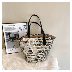 Detail of handwoven black and white straw tote bag with a large white lace bow accent