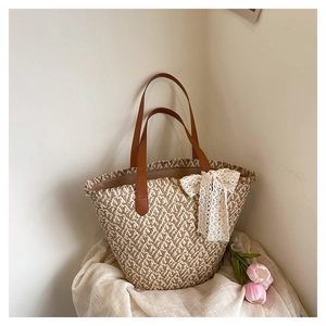 Close-up of woven straw tote bag featuring brown leather handles and lace bow accent