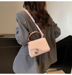 Dettaglio borsa in pelle verniciata rosa con fibbia a cuore argento su un blazer grigio
