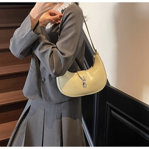 Detailed view of cream crescent shoulder bag with silver buckle worn with a gray blazer