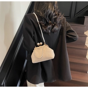 Detail of a beige woven clutch featuring large pearl clasps and a pearl chain strap