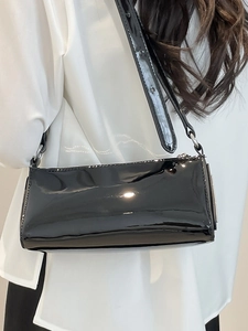 Chic black patent leather baguette bag with silver chain strap shown on shoulder