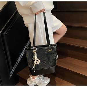 Detail einer schwarzen Beuteltasche mit Prägung, Goldösen und gewebtem Anhänger-Akzent