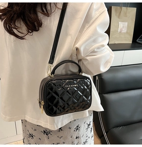 Détail du sac bandoulière en cuir verni noir avec texture matelassée et accents dorés